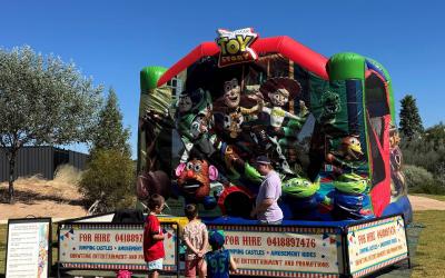 Children queue for Toy Story-themed bouncy castle under a clear blue sky.